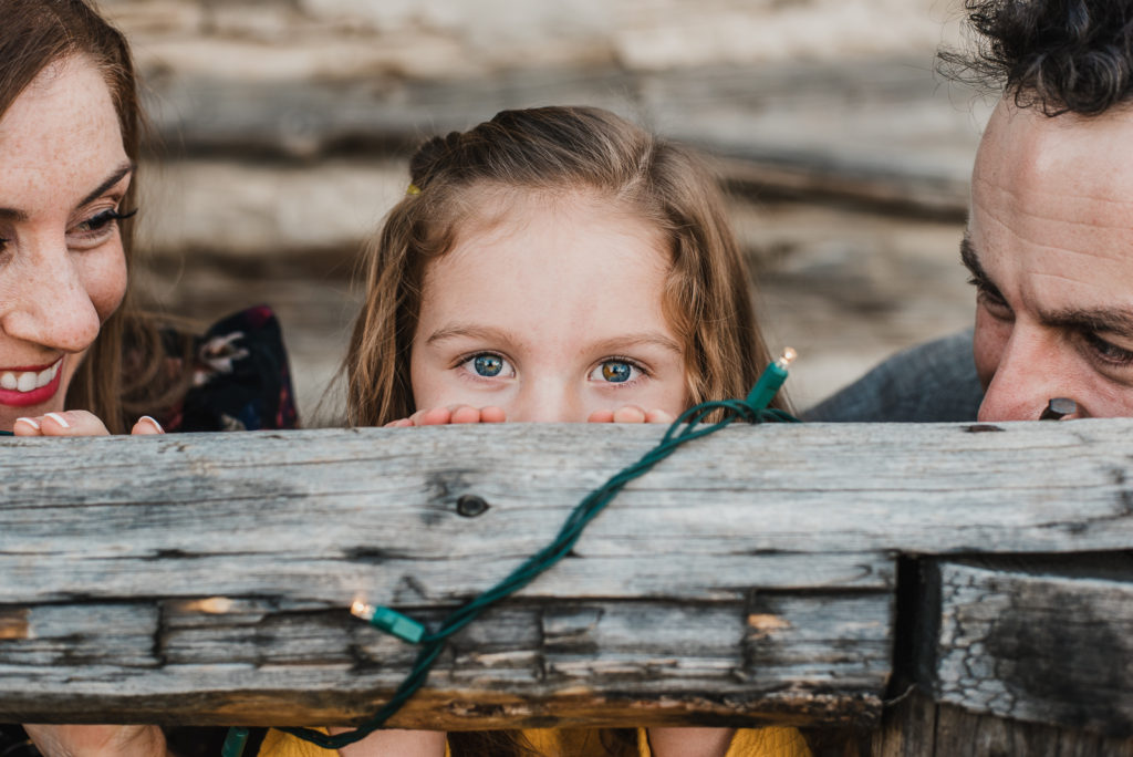 Little girl peeks above wooden board along with two parents