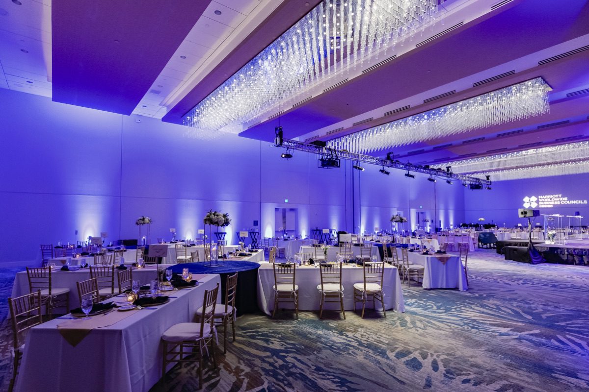 Grand ballroom with purple uplighting, crystal chandelier, and elegantly set banquet tables