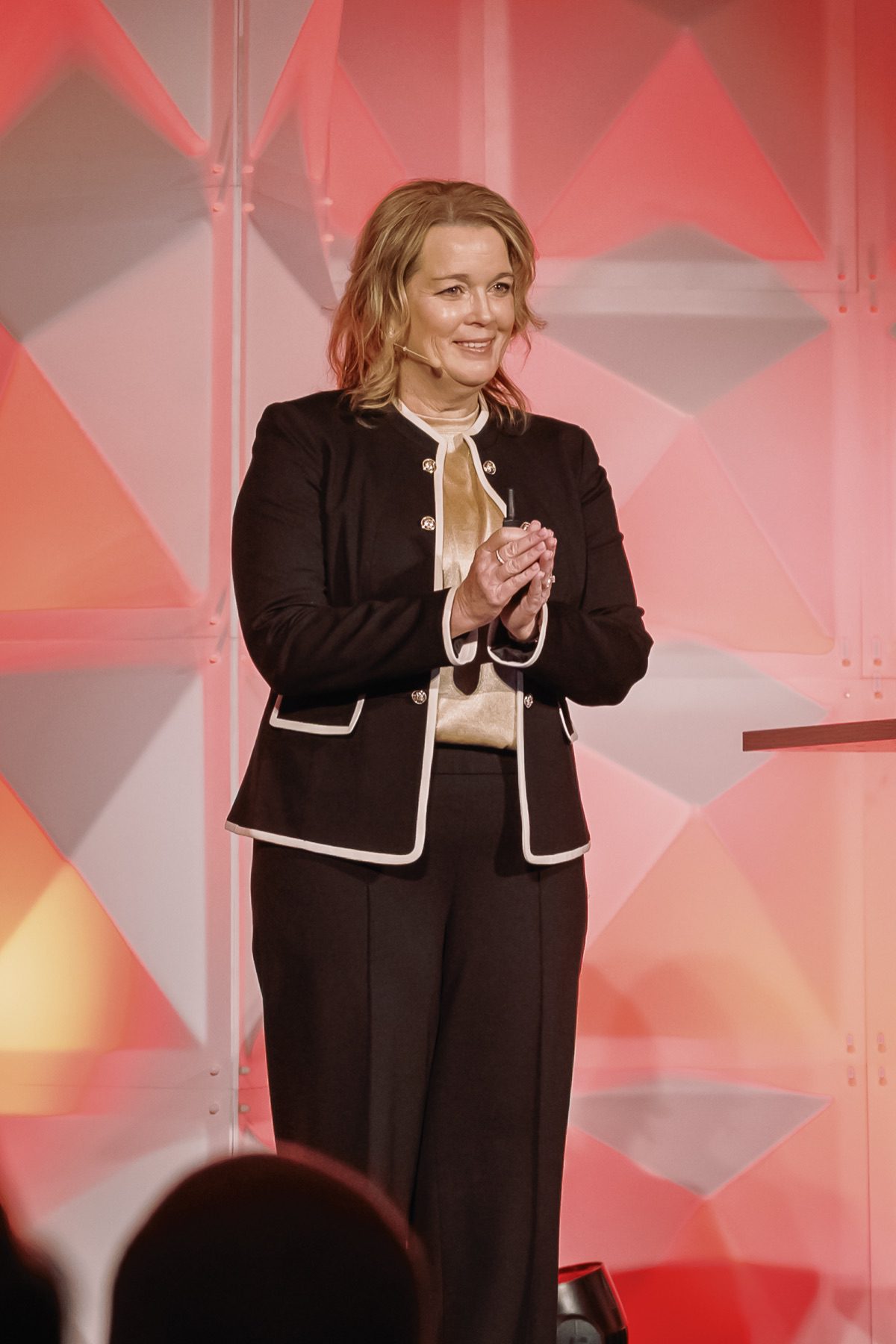 Female executive applauding on stage with geometric red and white backdrop