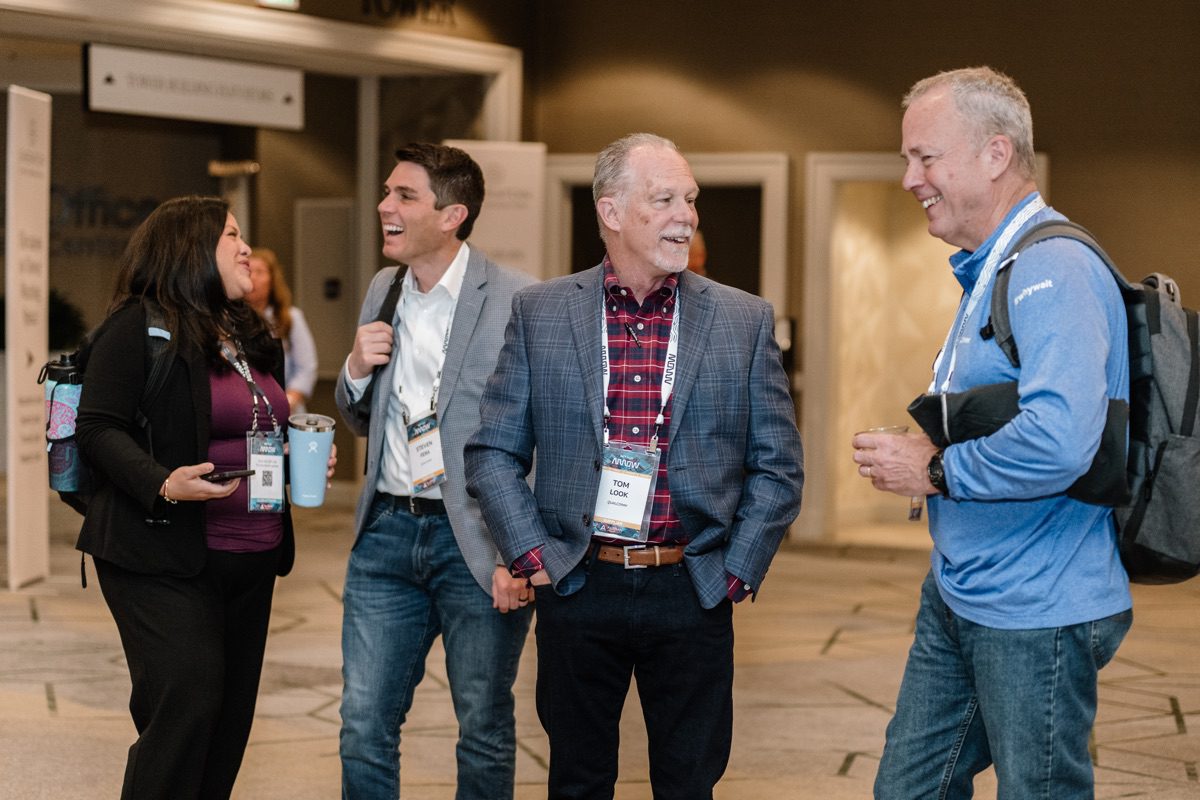 Four conference attendees laughing while walking through convention center hallway