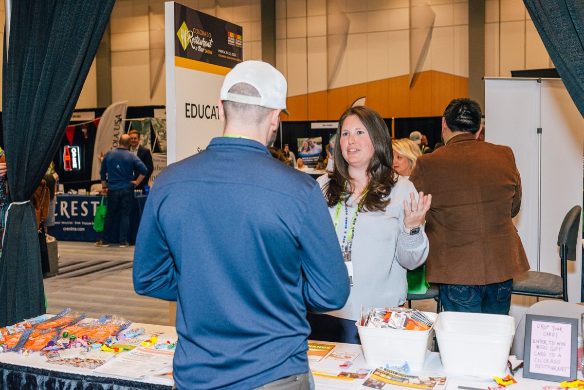 Expo floor booth conversation between exhibitor and attendee with brochures and swag