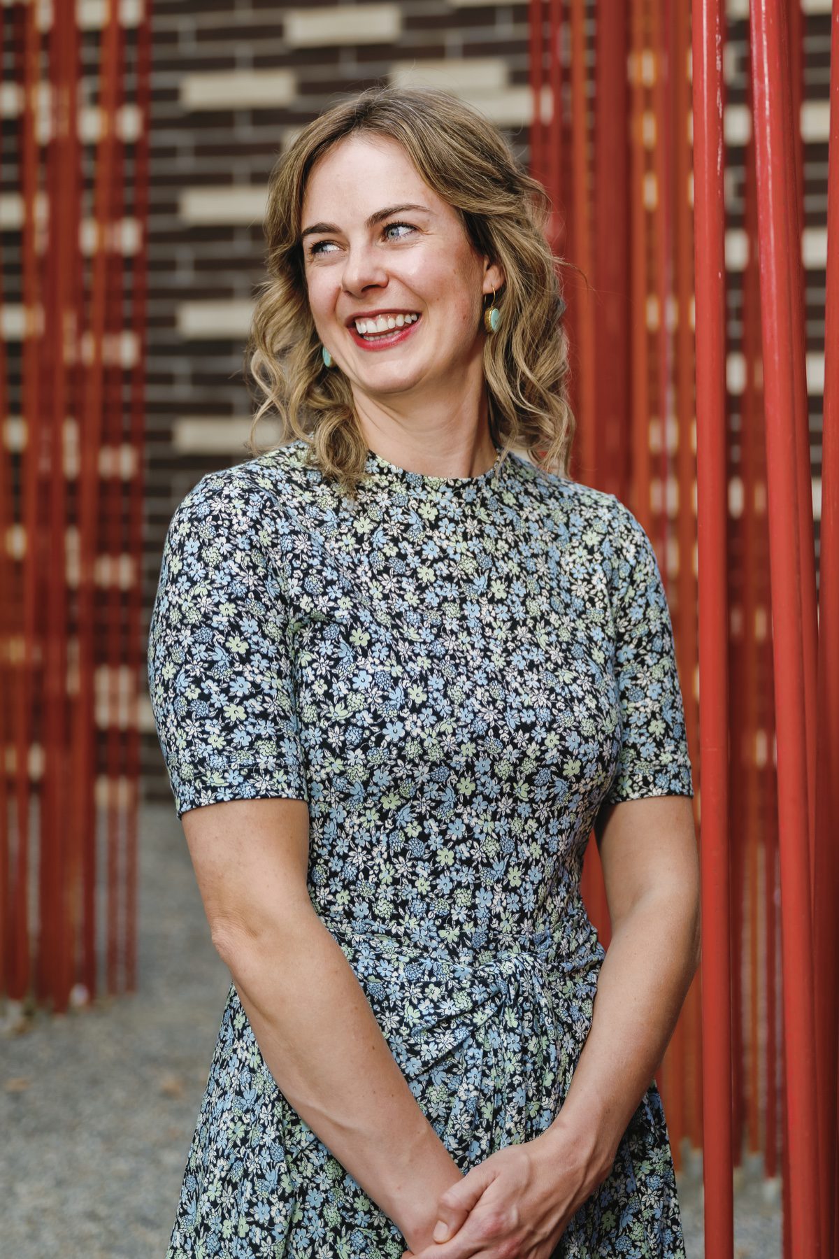 Laughing woman in floral dress beside vibrant red architectural columns outdoors