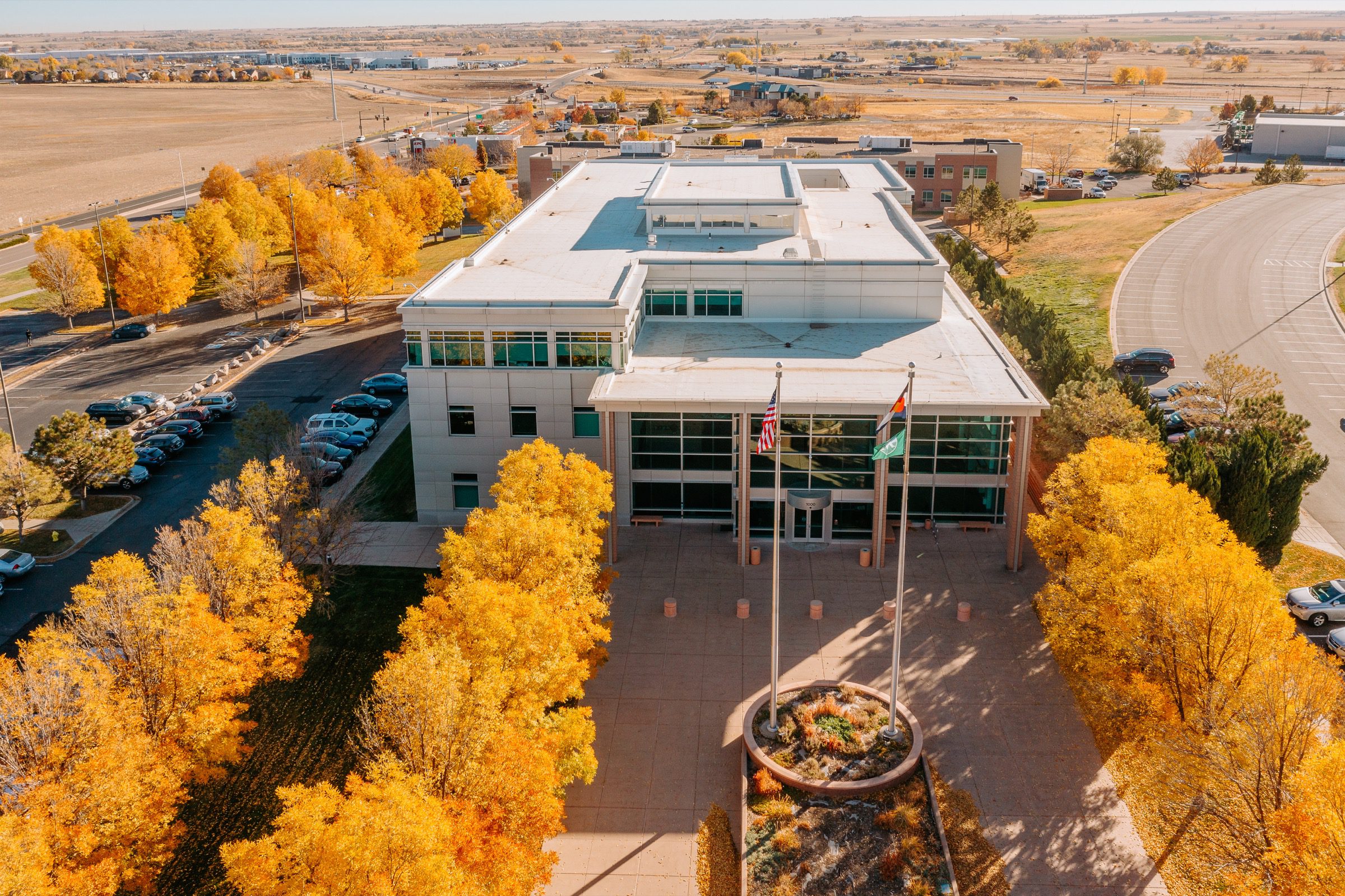 Aerial view of commercial building entrance with golden fall foliage and flags