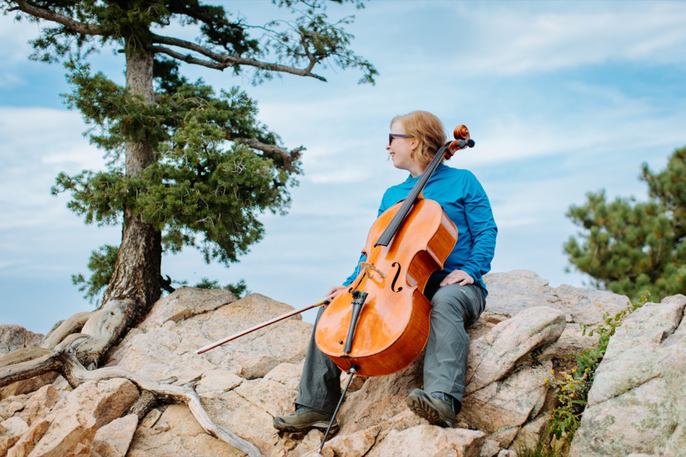 Cellist on a granite ridge with windswept pines, Front Range backdrop