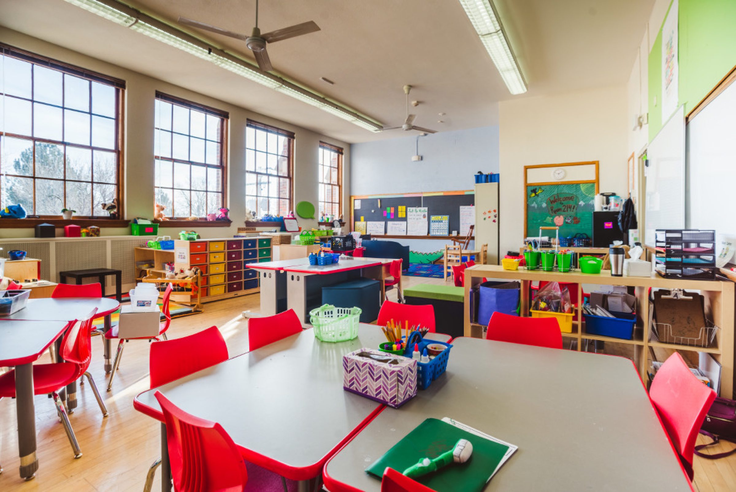 Bright color-everywhere classroom -- red chairs, supply bins, tall windows