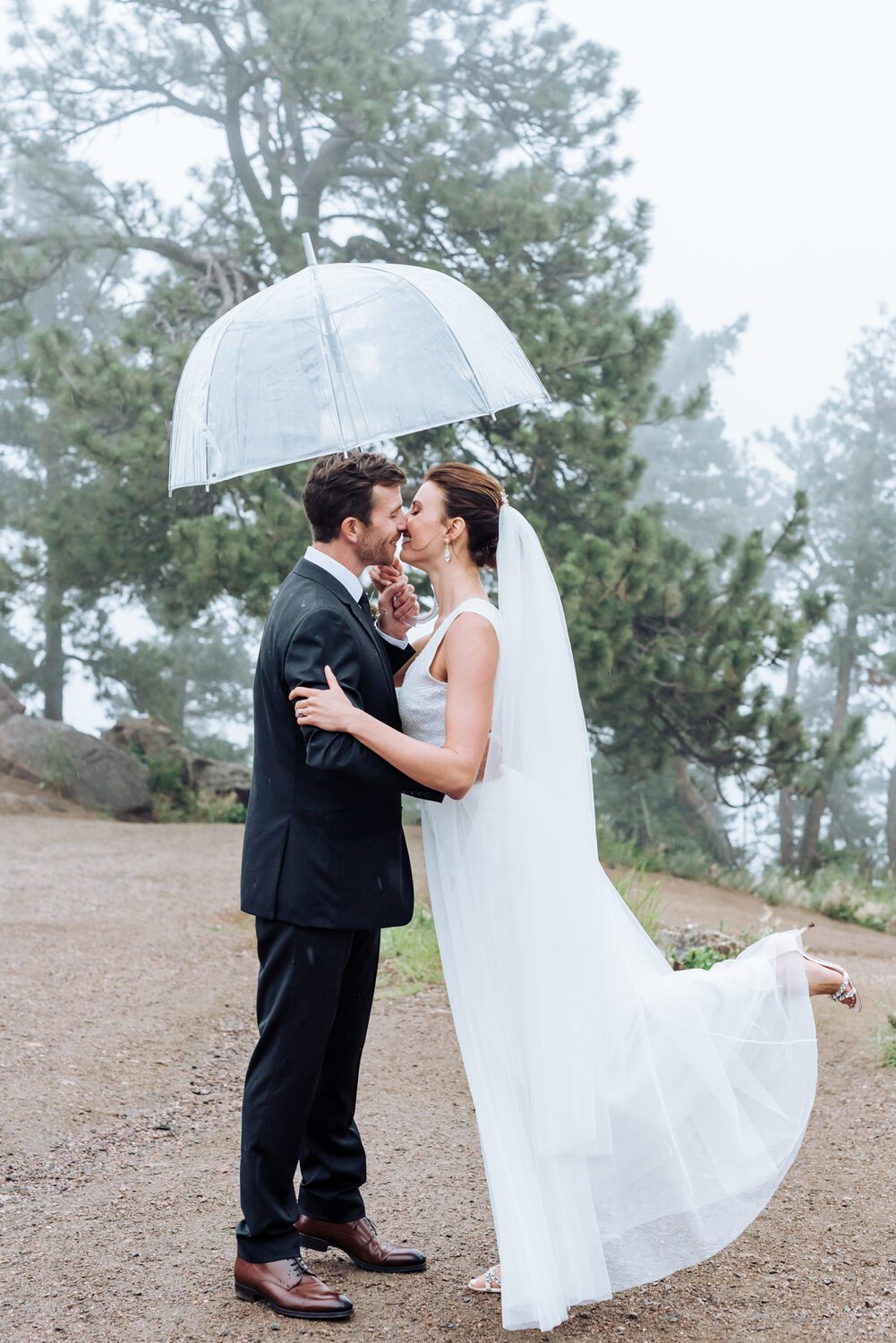 Bride and groom under a clear umbrella in the mountain mist at Boettcher Mansion