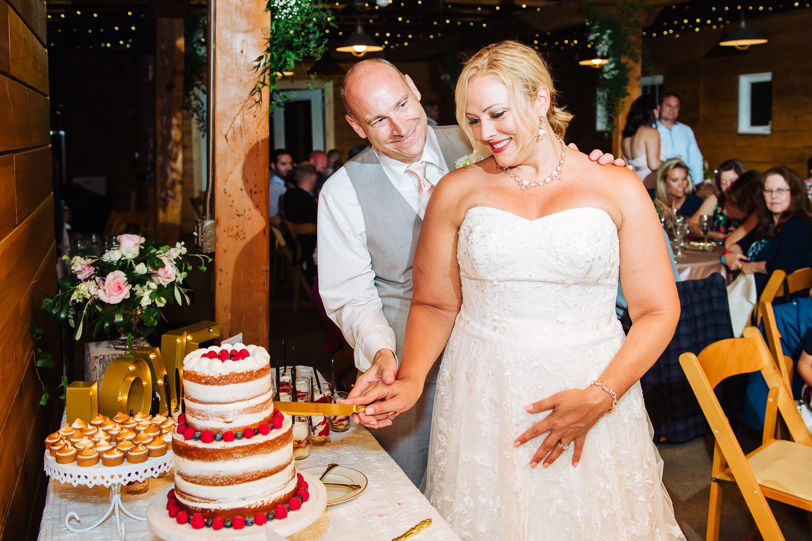 Newlyweds cutting the cake at a barn reception under string lights at Chatfield Farms