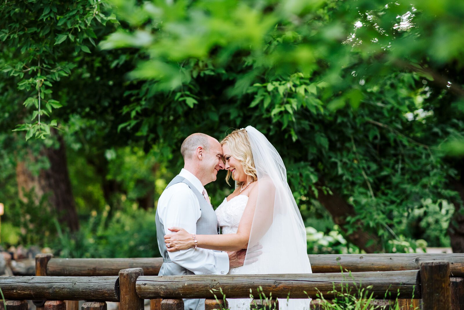 Couple embracing on a wooden bench framed by summer greenery at Chatfield Farms