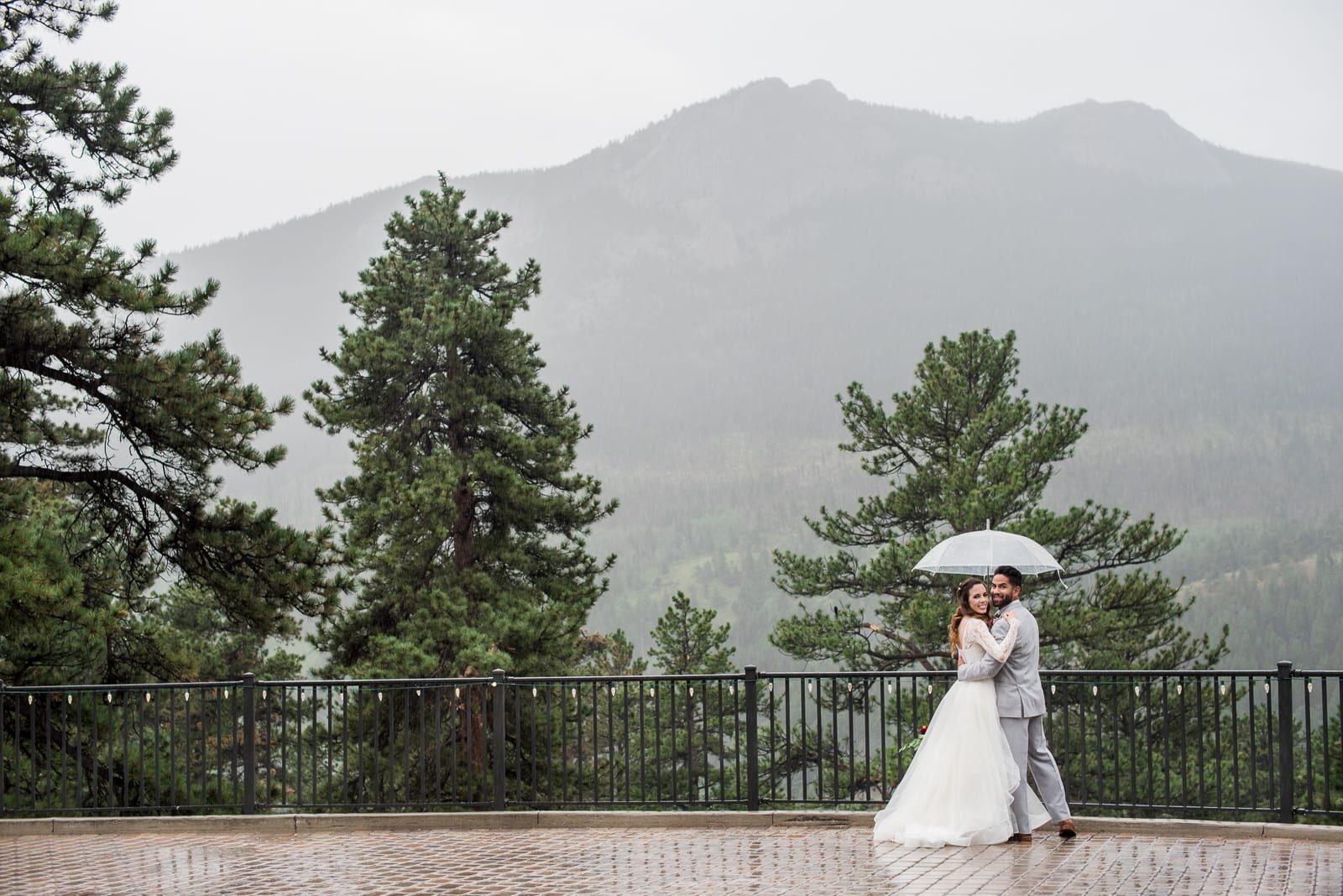 Bride and groom under an umbrella on the terrace at Della Terra Mountain Chateau, the misty peaks beyond