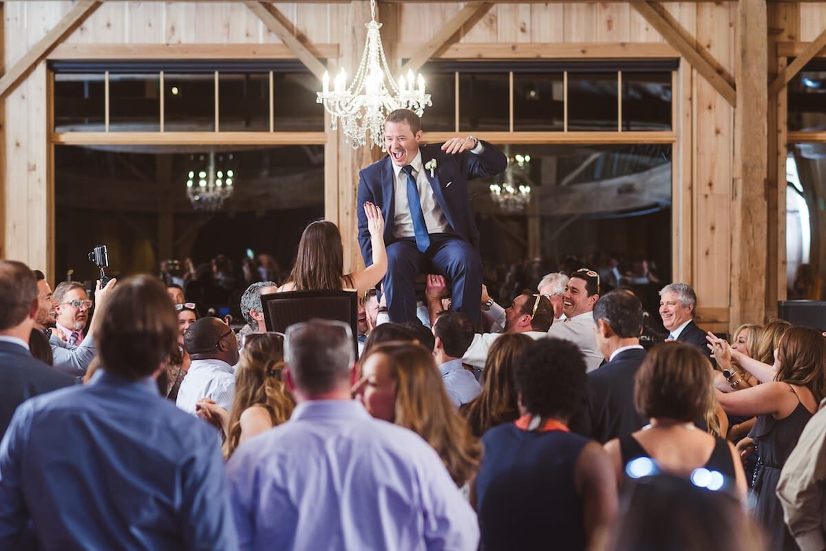Guests lifting a groomsman during the reception under the chandeliers in High Lonesome Barn at Devil's Thumb Ranch