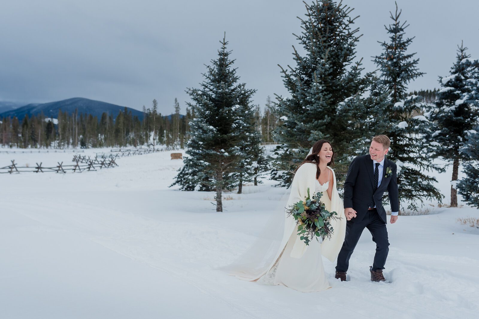 Bride and groom walking through snow among the spruces at a winter Devil's Thumb Ranch wedding