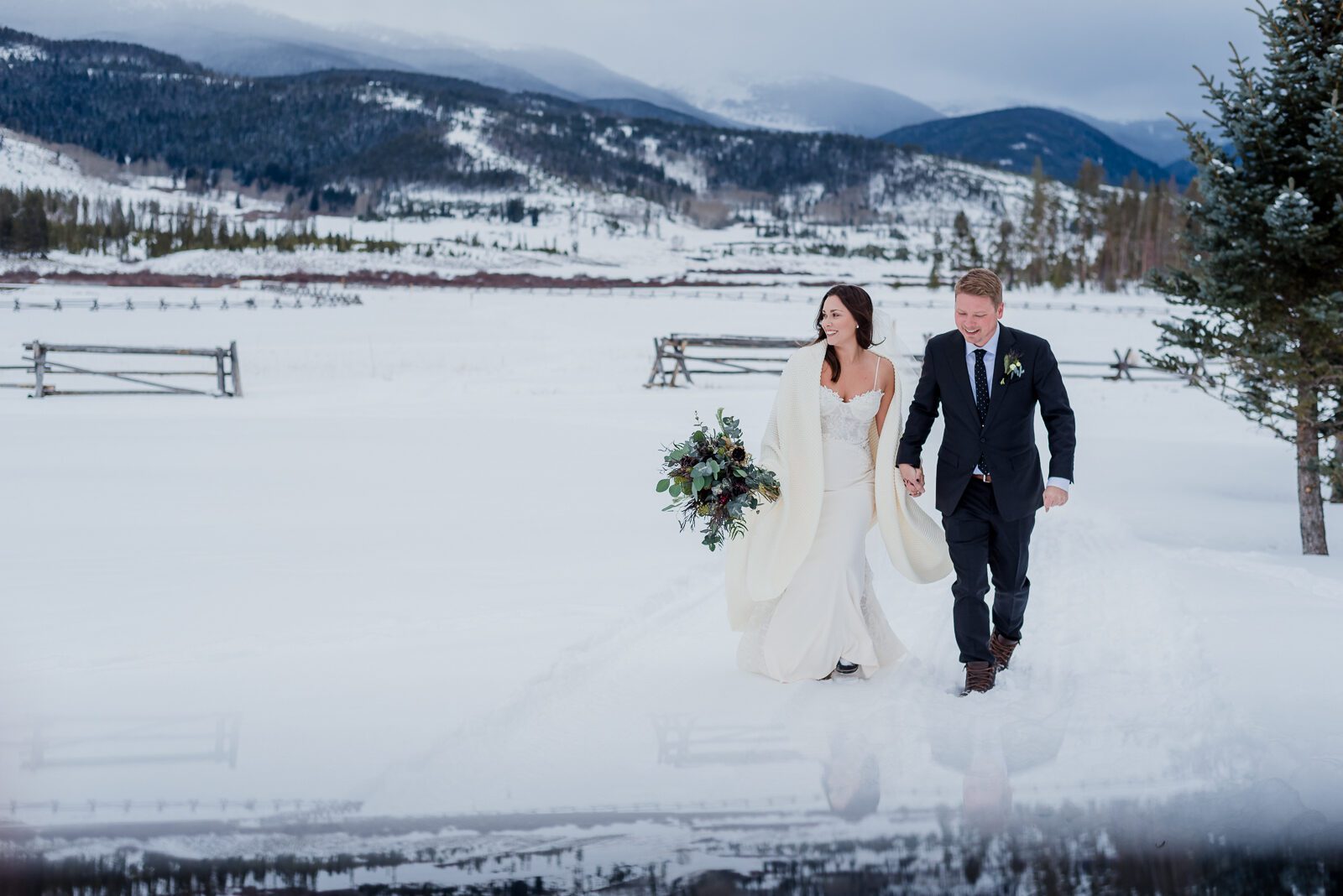Bride and groom walking through deep snow with the Divide behind them at a winter Devil's Thumb Ranch wedding