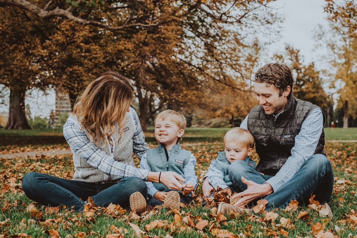 Family of four sitting in fallen autumn leaves under the trees at Cheesman Park, Denver