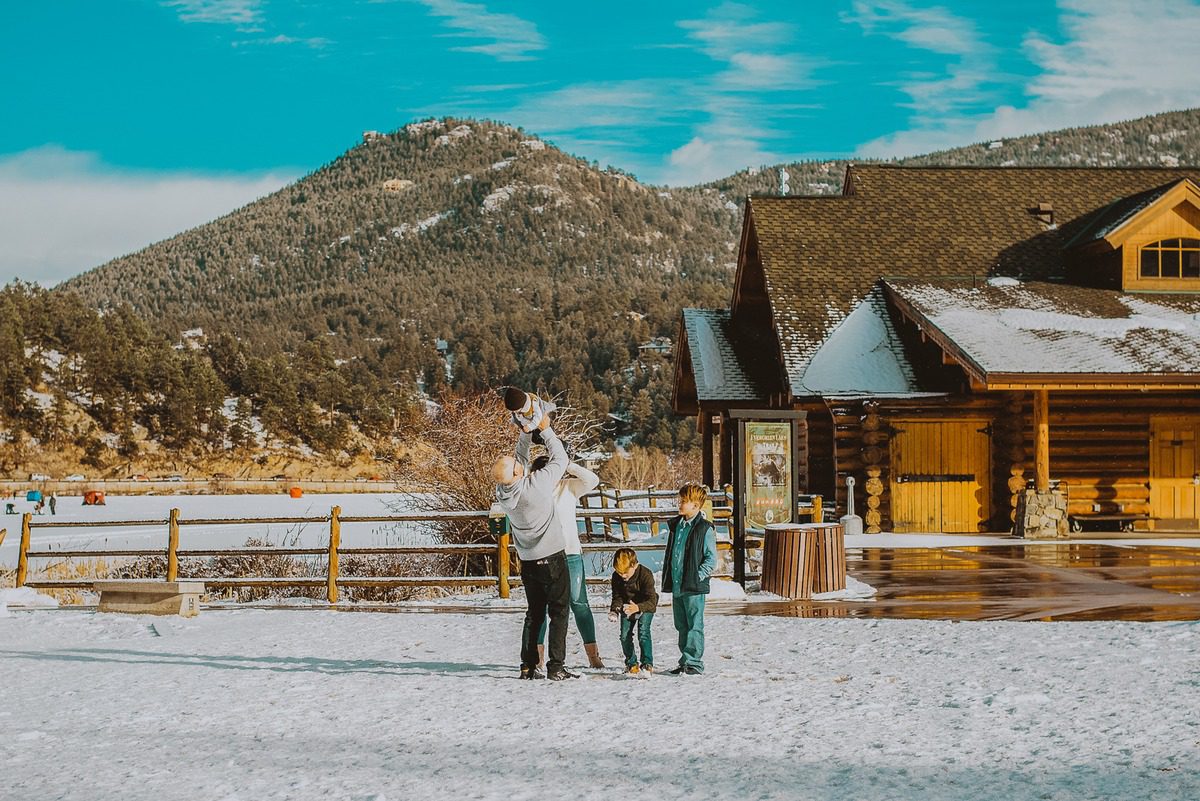 Family in the snow outside the log Evergreen Lake House in Colorado
