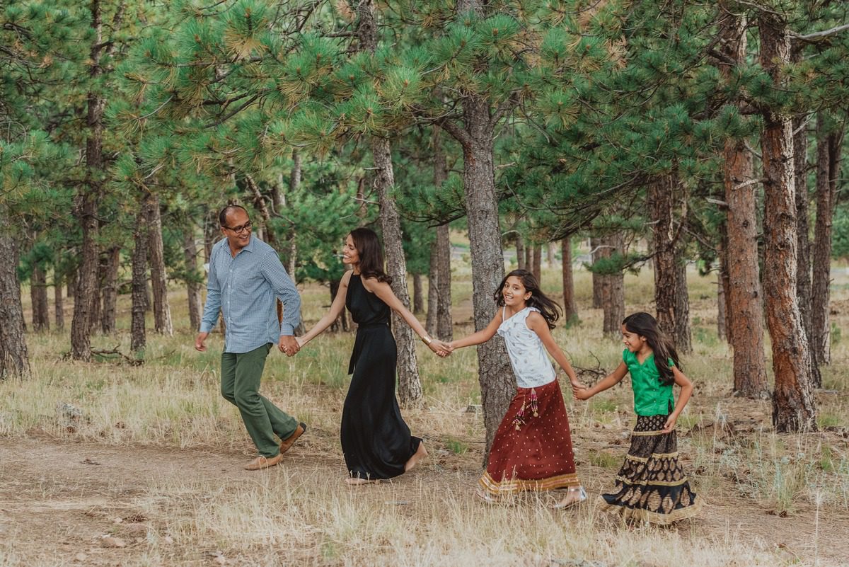 Family of four walking hand in hand through the pines on Lookout Mountain, Colorado