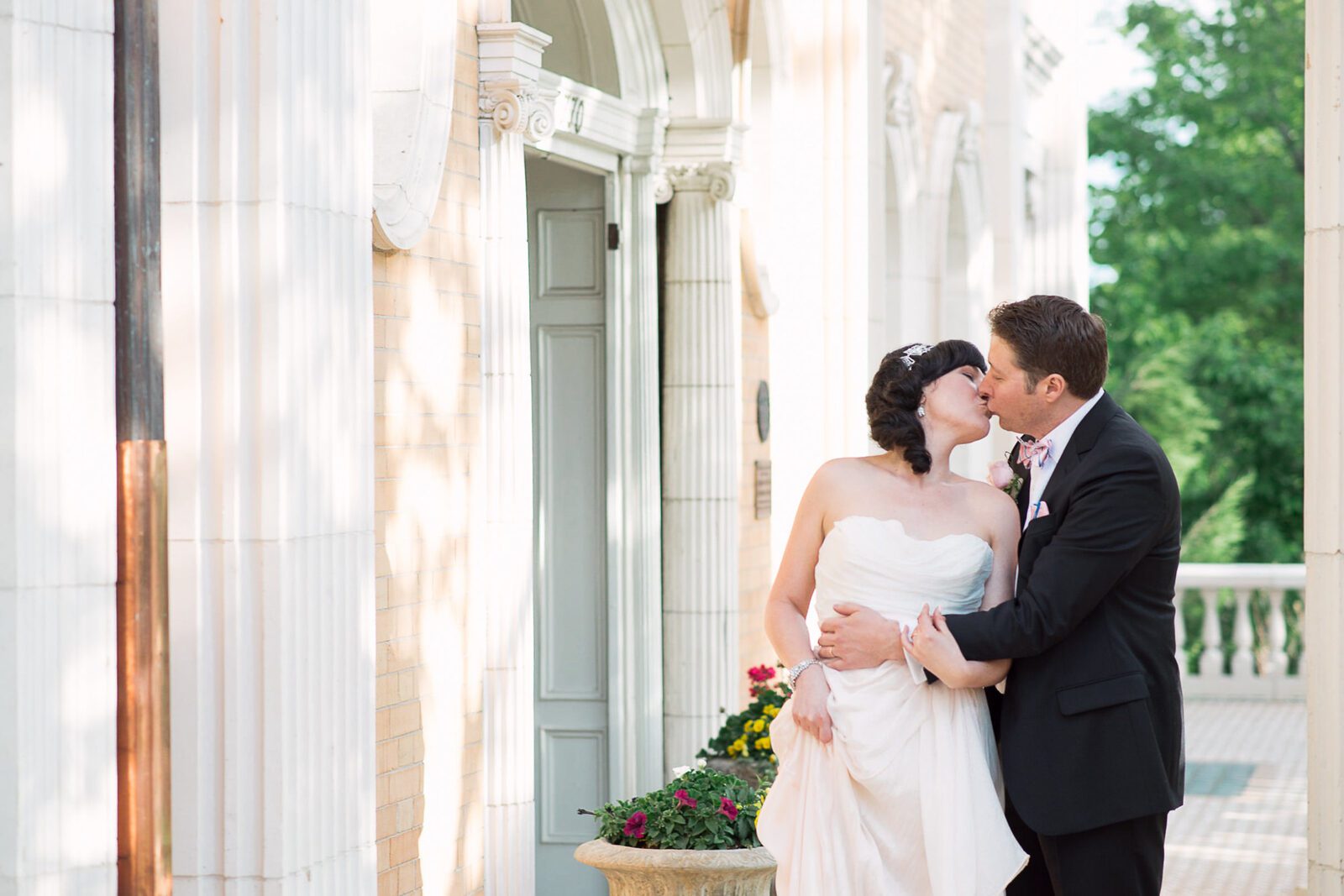 Bride and groom kissing between the Beaux-Arts columns on the veranda at the Grant-Humphreys Mansion