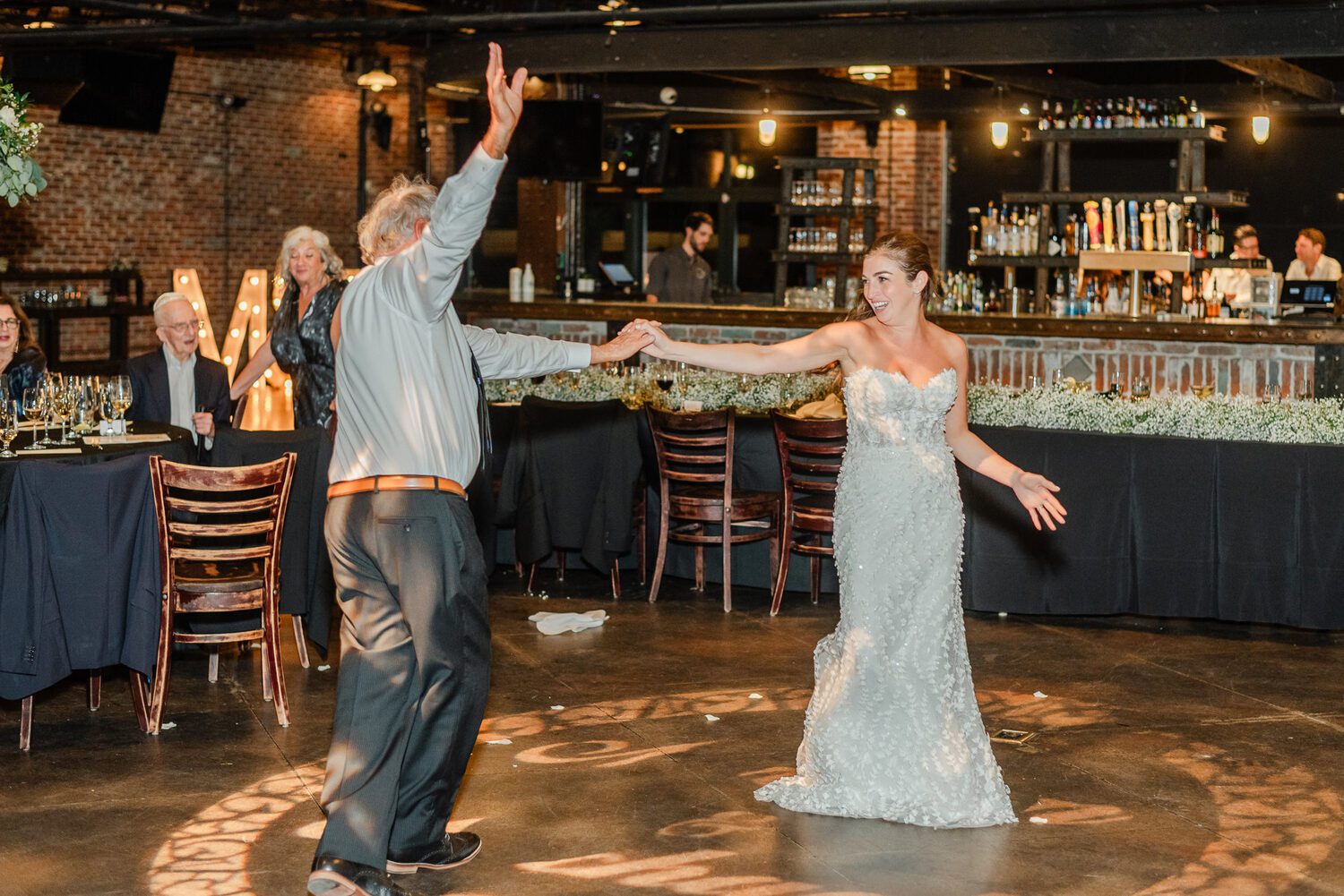 A father-daughter dance in front of the long bar at Mile High Station, exposed brick and the mezzanine above