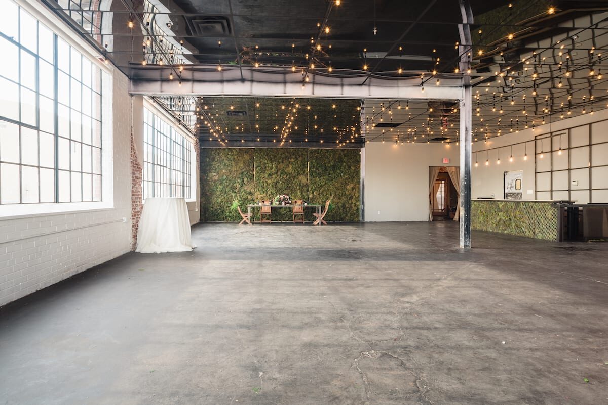 The main room at Moss Denver: concrete floor, steel-framed windows, string lights and the moss wall