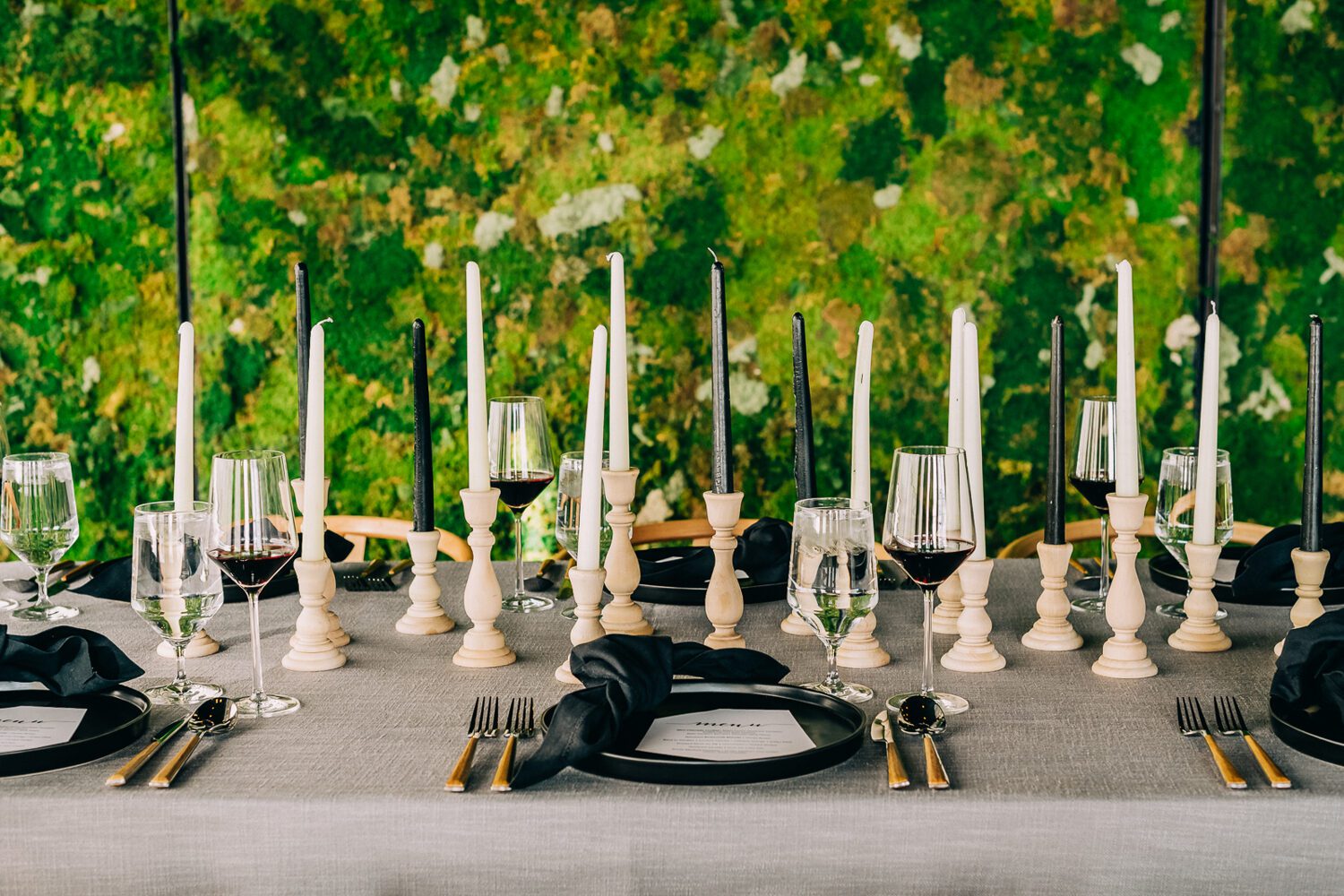 A long table set with black tapers and gold flatware against the moss wall at Moss Denver