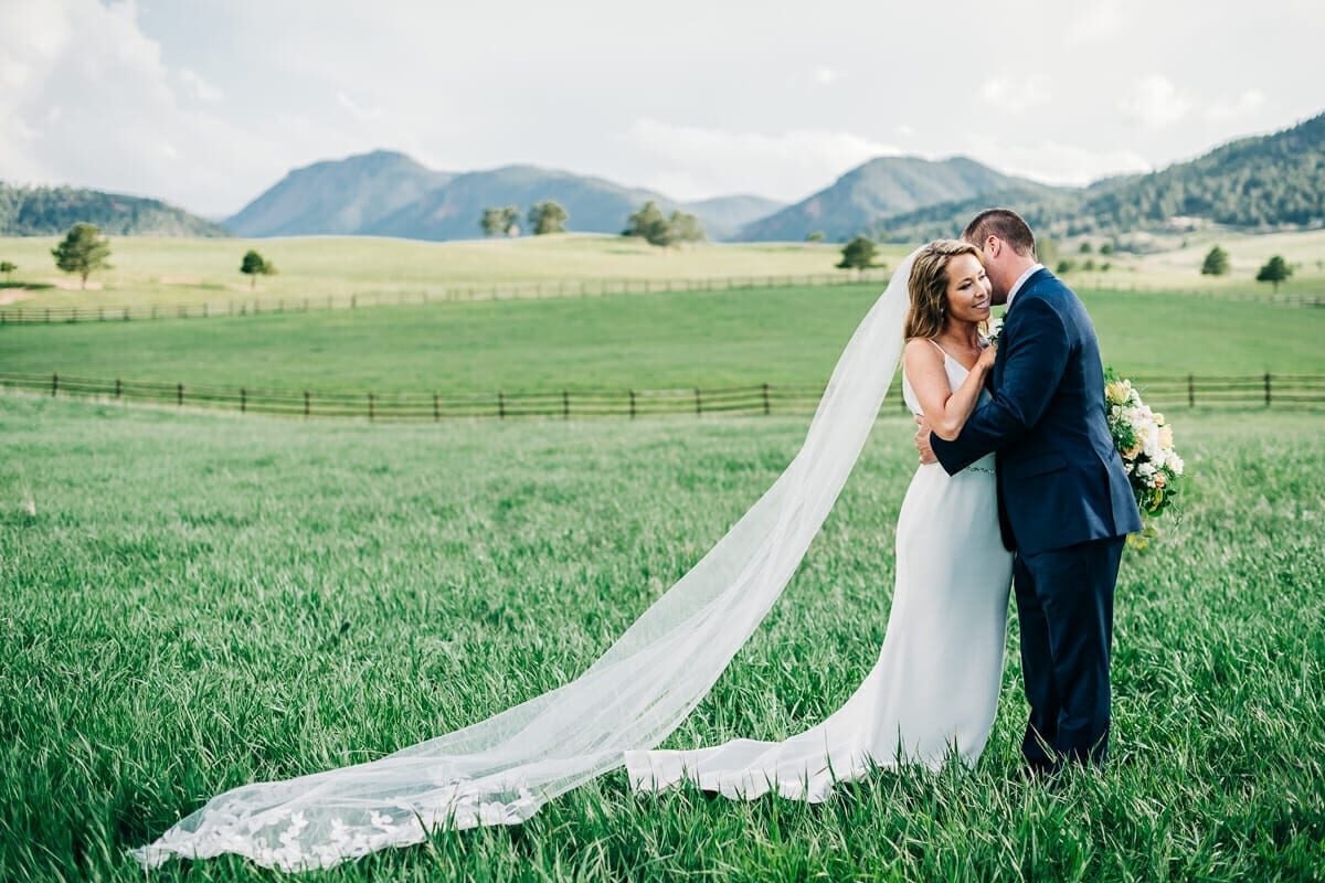 Bride's long veil trailing across the meadow with the mountain range behind at Spruce Mountain Ranch