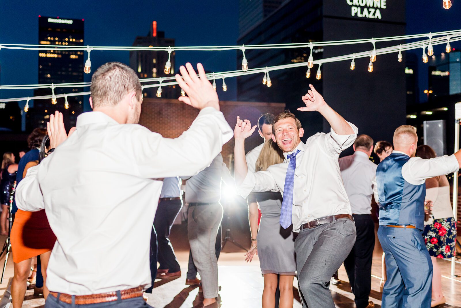 Guests dancing under string lights on the rooftop sundeck, downtown Denver behind them