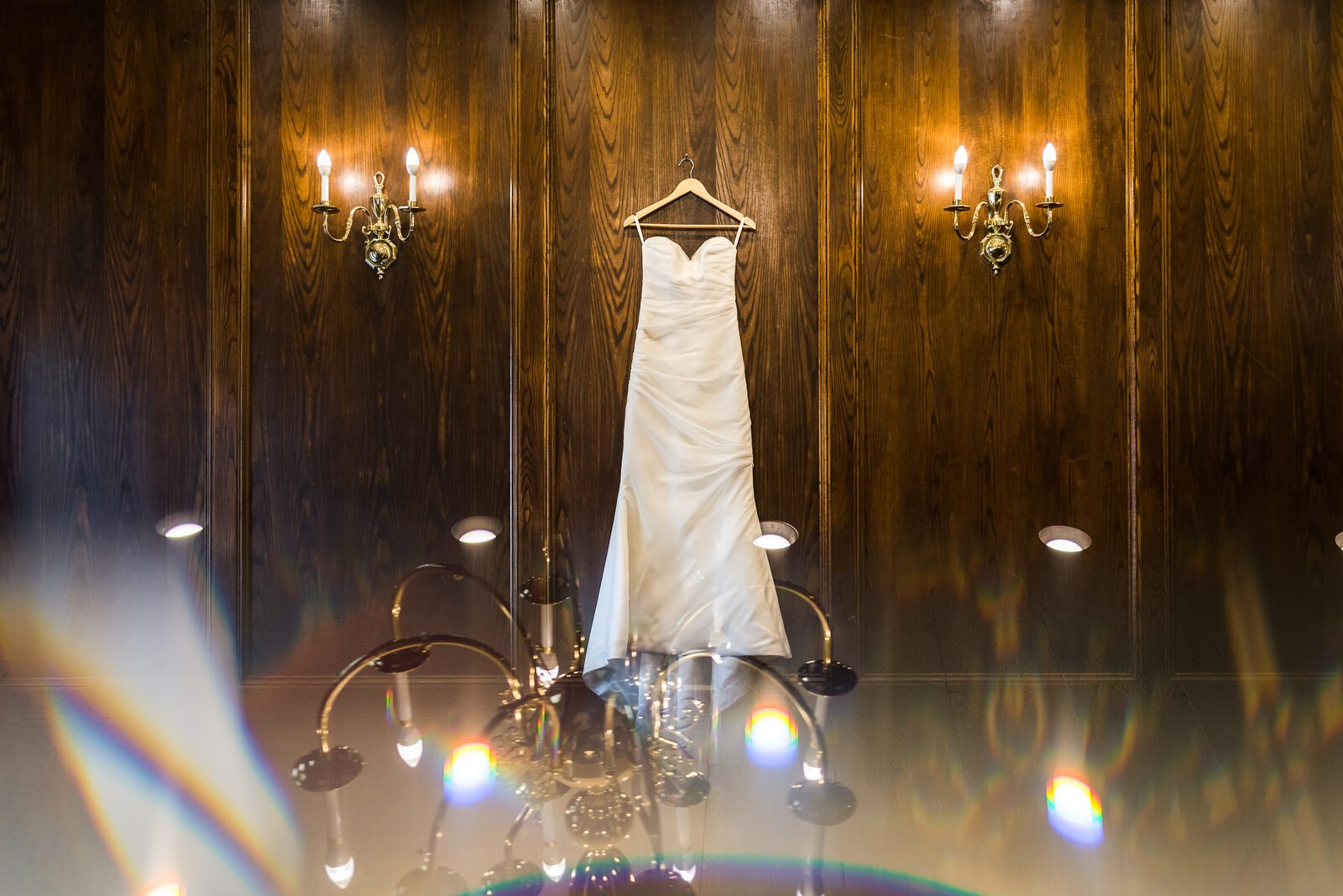 The wedding dress hanging against the wood panelling at the Denver Athletic Club, a sconce either side