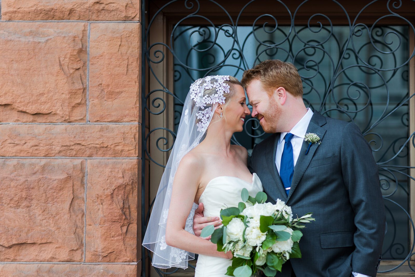Bride and groom beside the ornate ironwork and red sandstone at the Denver Athletic Club